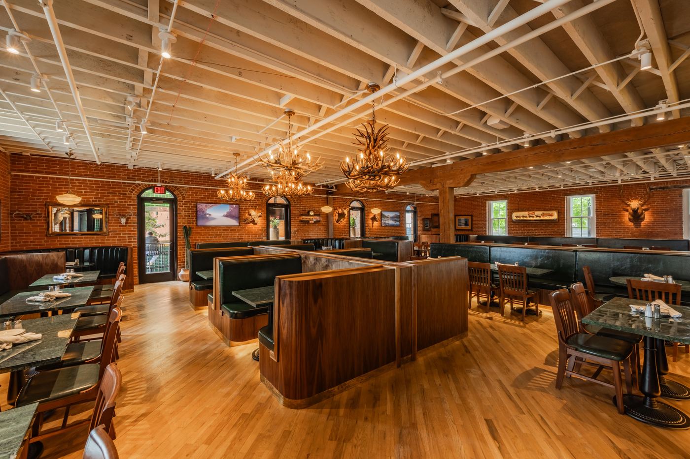 Main dining room at Culpepper Cattle Co. with antler chandeliers, exposed brick, and green leather booths
