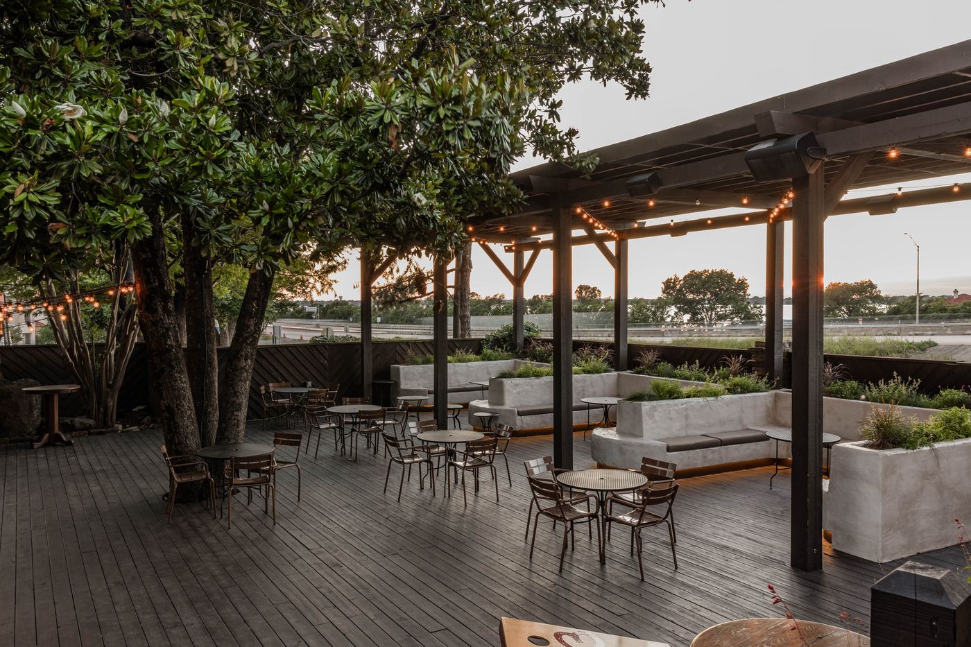 Renovated patio at Culpepper Cattle Co. Rockwall with pergolas, plaster banquettes, and planters under mature magnolias
