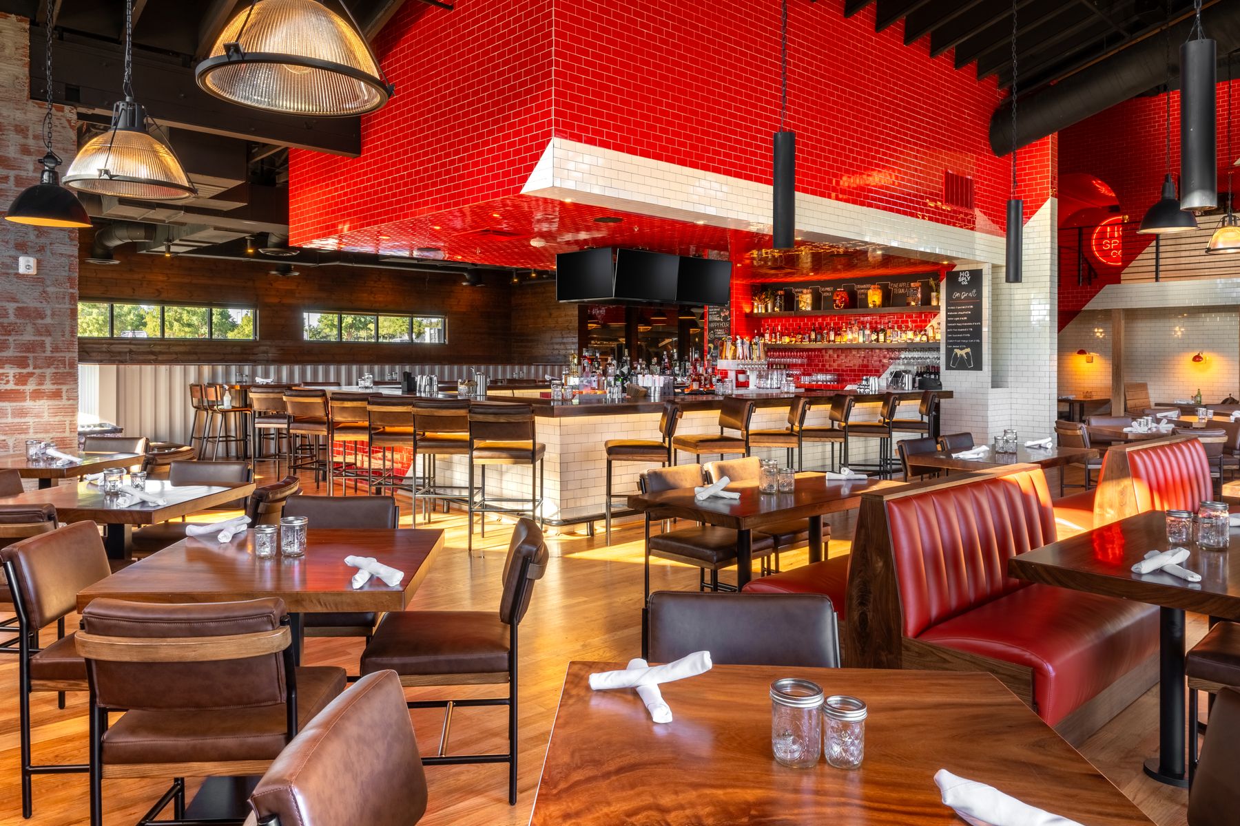Bar and dining room at HG Sply Co. Alliance with glazed red subway tile, walnut tables, and leather seating