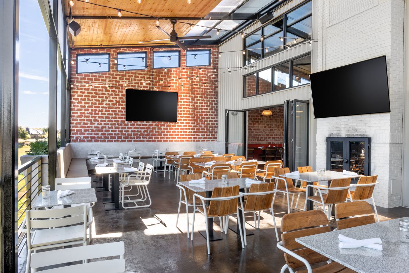 Covered patio at HG Sply Co. Alliance with painted brick, string lights, and a fireplace