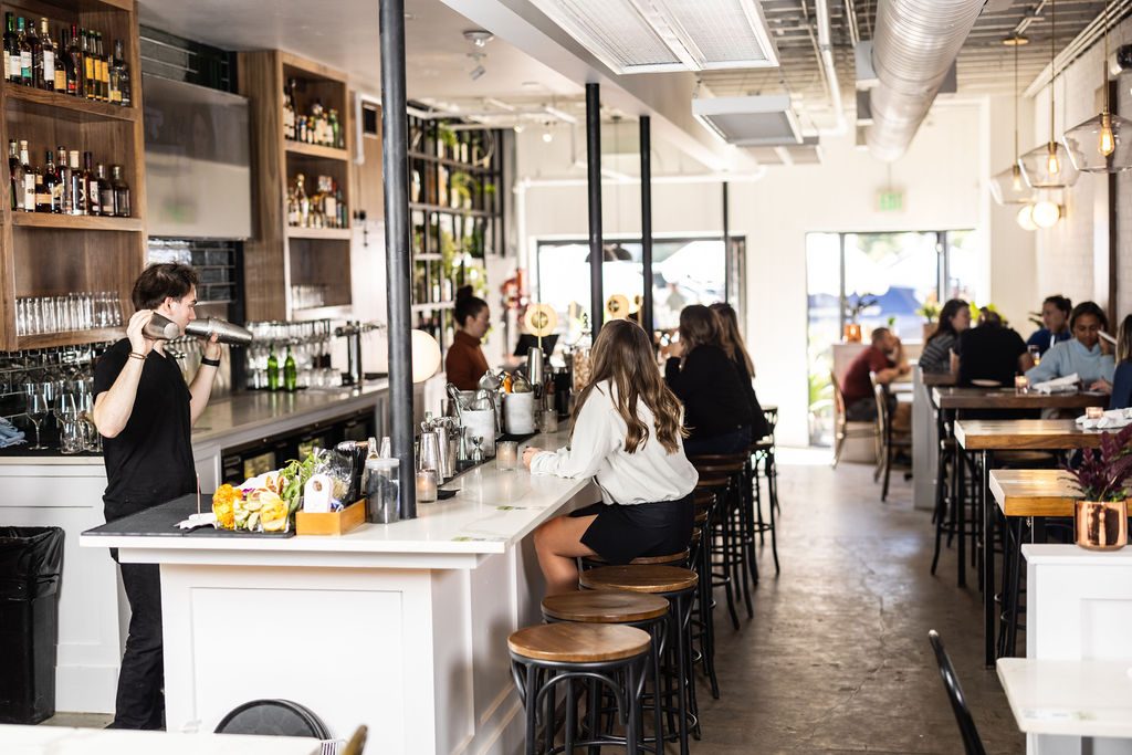Bartender working the bar at Leela's wine bar on Lower Greenville, with guests seated on wood stools